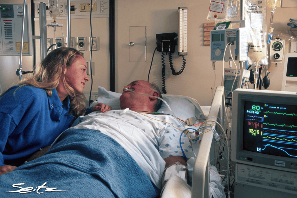 A young woman visits an elderly hospital patient in a hospital bed. © Blair Seitz
