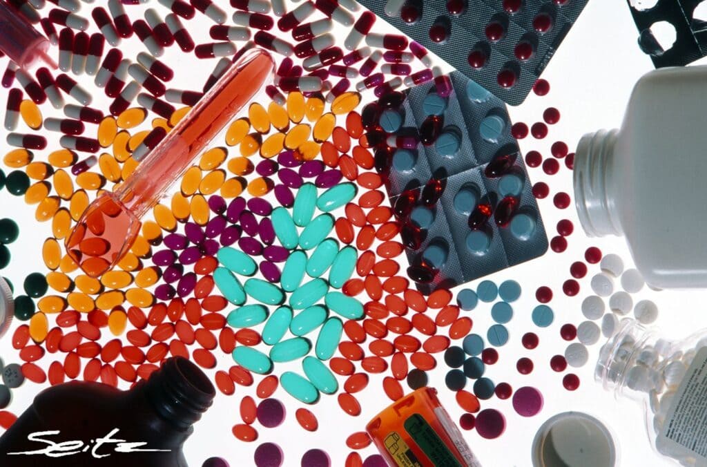 Pills spill out of pill bottles on a white surface. © Blair Seitz