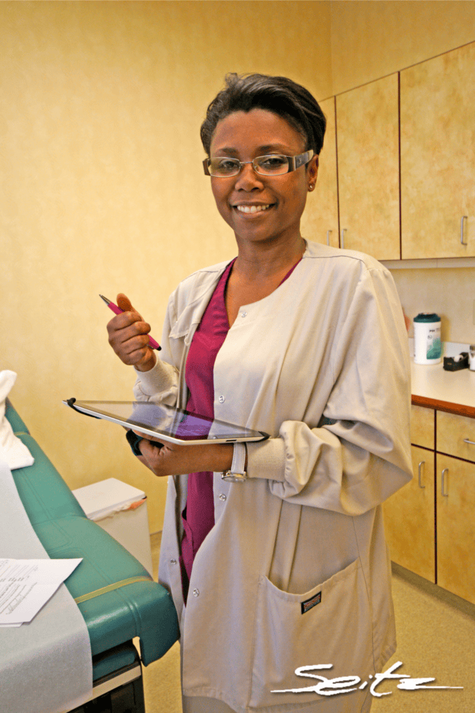 Black/African American nurse uses tablet to access patient records in exam room. © Blair Seitz